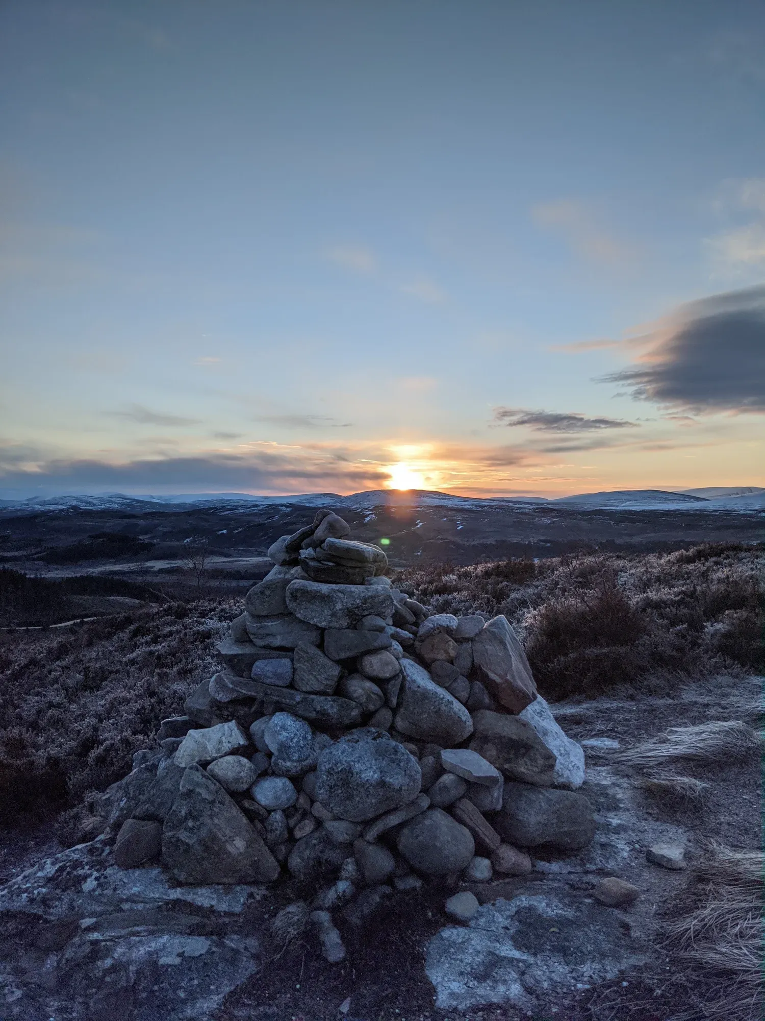 Glentruim Viewpoint cairn at winter sunrise — snow on the hills, low warm sun